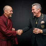 photograph, studio portrait of a balding man in an earthy red monk's robe and a gray-haired man in a pinstriped suit shaking hands, both laughing, monk holding prayer beads, suited man holding a whiskey glass and cigar, wearing heavy gold chains, rings, and watch, and a golden crest on his blazer, low-key lighting, shallow depth of field, dark background