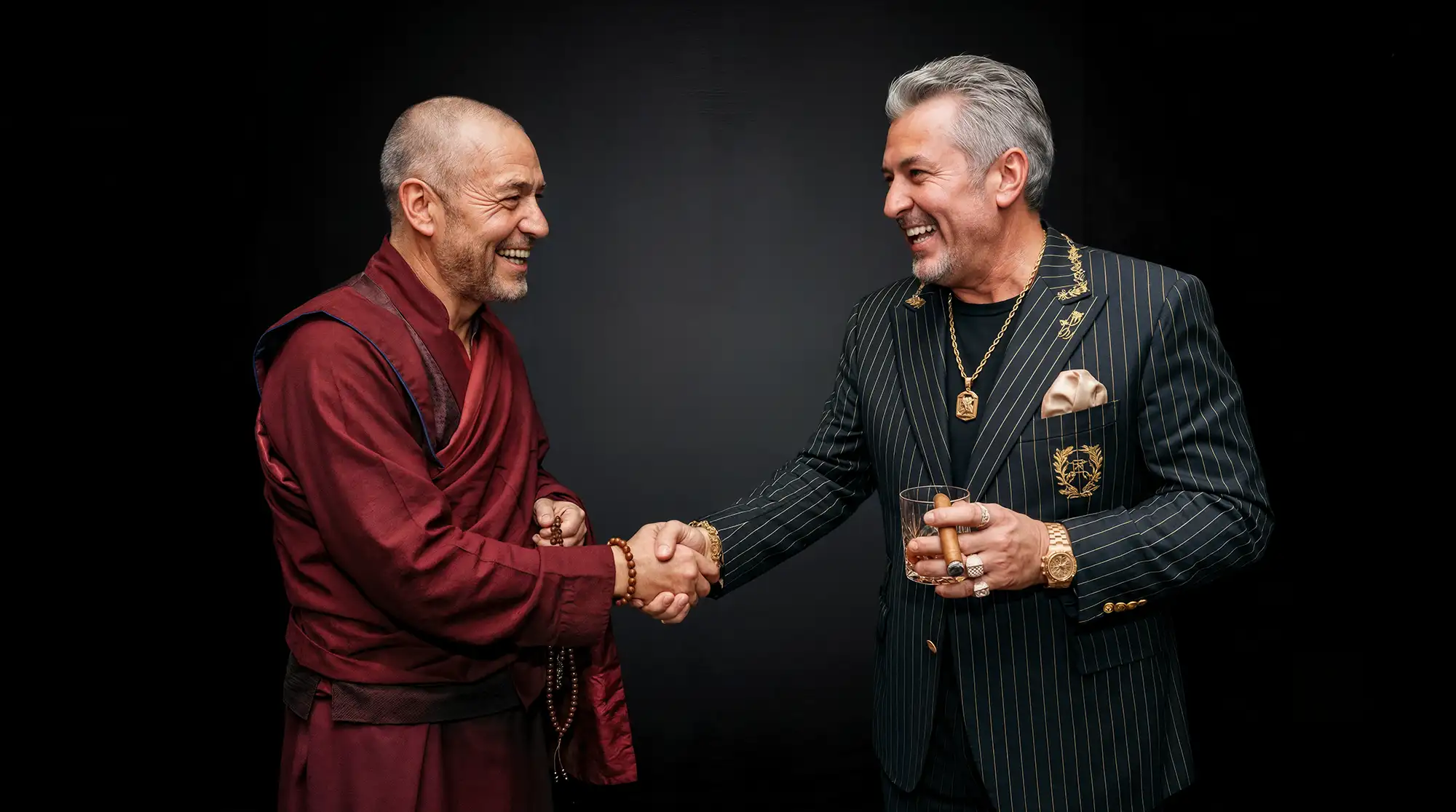 photograph, studio portrait of a balding man in an earthy red monk's robe and a gray-haired man in a pinstriped suit shaking hands, both laughing, monk holding prayer beads, suited man holding a whiskey glass and cigar, wearing heavy gold chains, rings, and watch, and a golden crest on his blazer, low-key lighting, shallow depth of field, dark background